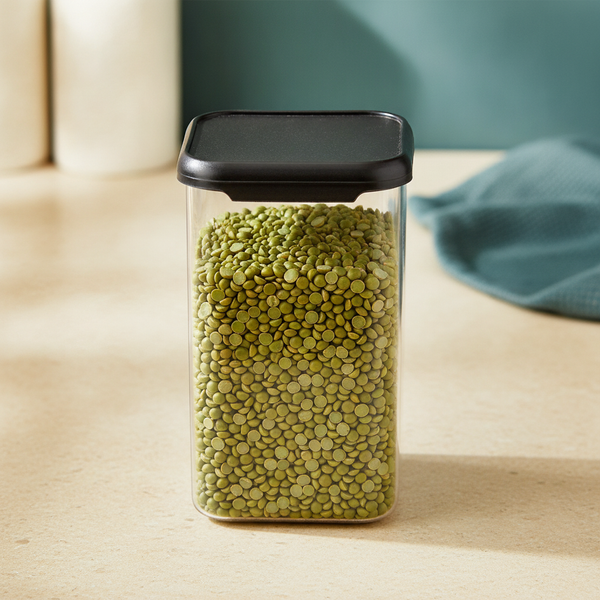 Top-down view of a clear, BPA-free airtight storage container filled with green lentils on a cream counter, highlighting mate